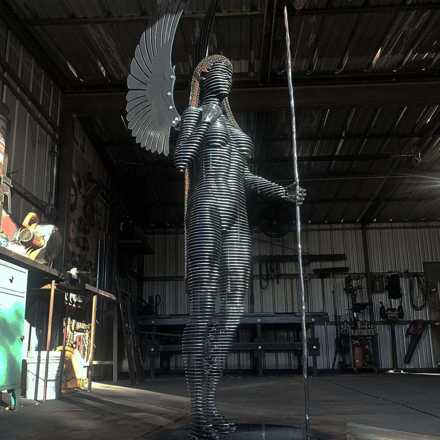 Eternal, a life-size angel of stacked horizontal steel slices, standing in John's Tucson workshop with a polished wing above her shoulder